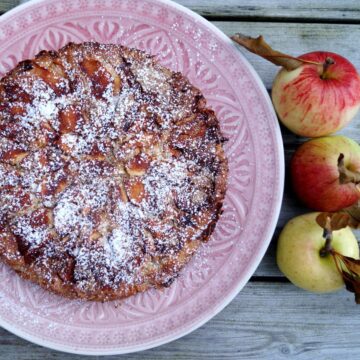 Bagt æblekage med kardemomme og chokolade og drysset med flormelis på kagefad